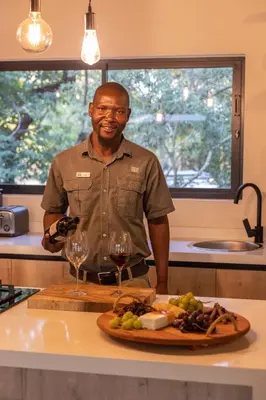 a man standing in a kitchen with a plate of food and wine glasses at Ukanyi Private Luxury Villa in Hoedspruit