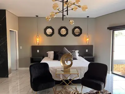 a bedroom with a bed with two chairs and two mirrors at Swan Lake Suites in Benoni