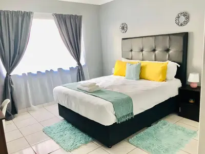 a bedroom with a large bed with yellow and blue pillows at Menlyn Comfort in Pretoria