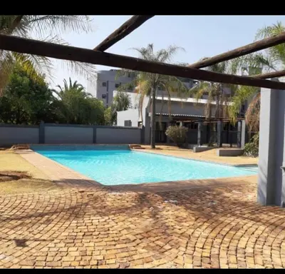 a large blue swimming pool with a building and palm trees at Menlyn Comfort in Pretoria
