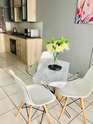 a glass table with white chairs and a vase of flowers at Menlyn Comfort in Pretoria