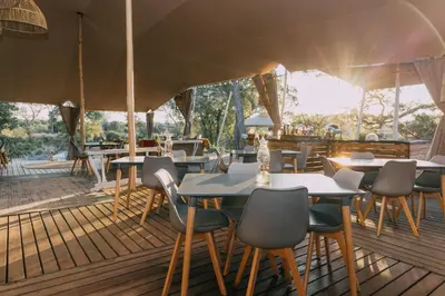 a restaurant with tables and chairs under an umbrella at Kruger Untamed - Tshokwane River Camp in Skukuza