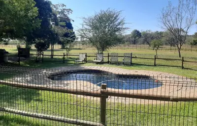 a pond in a field with two chairs and a fence at Matalatala Wildlife Lodge in Roodeplaat