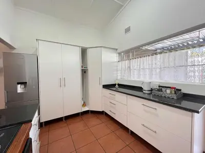 a kitchen with white cabinets and a black counter top at Palm House Accomodation in White River