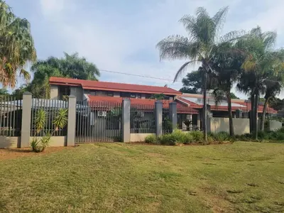 a fence in front of a building with palm trees at Hoep Hoep Self Catering in Groblersdal
