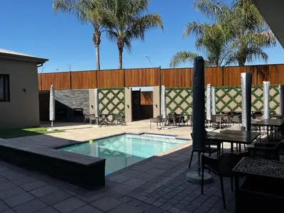 a swimming pool with tables and chairs and palm trees at Riverleaf Hotel in Brits