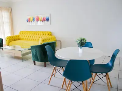 a dining room with a table and chairs and a yellow couch at 11 The Blyde Crystal Clear Lagoon 2 Bedroom Garden Apartment in Pretoria