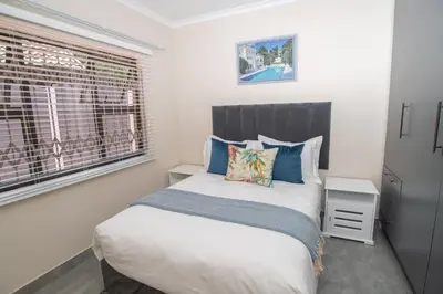 a bedroom with a bed with blue pillows and a window at Colourfully cosy in Pretoria