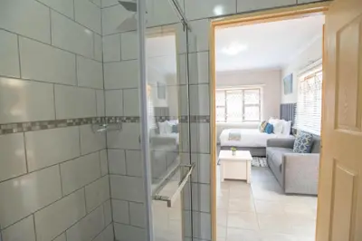 a bathroom with a shower and a living room at The Blue & Grey Nest in Pretoria
