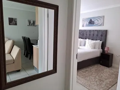 a mirror reflecting a bedroom with a bed and a chair at THE BLYDE Holiday Apartments in Pretoria