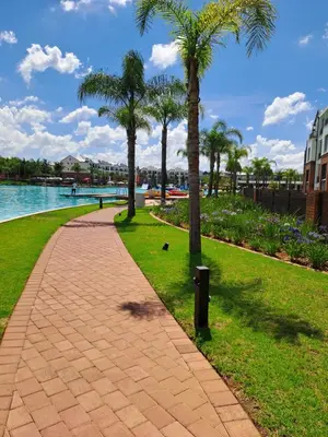 a walkway next to the water with palm trees at THE BLYDE Holiday Apartments in Pretoria