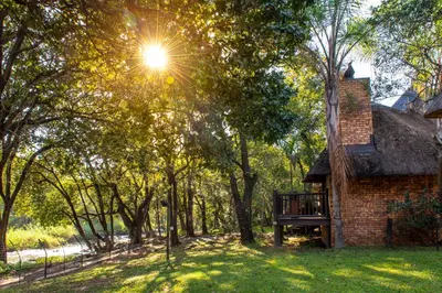 a brick house with the sun shining through the trees at Kruger Park Lodge Unit No. 209 in Hazyview