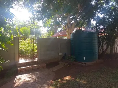 a fence with a water tank next to a tree at Africa Dawn Guesthouse in Musina