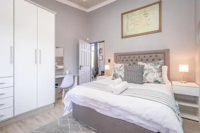 a white bedroom with a large bed and a desk at Dorpshuis in Dullstroom