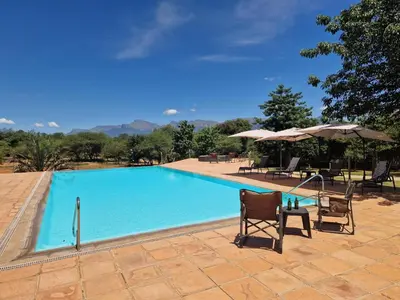 a swimming pool with two chairs and an umbrella at Thandolwami Bushlodge in Hoedspruit