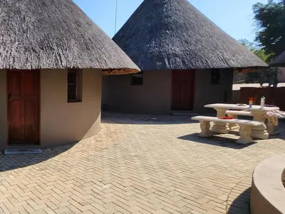 two huts with thatched roofs and a picnic table in front at Thandolwami Bushlodge in Hoedspruit