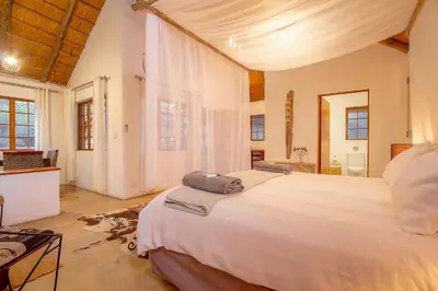a bedroom with a large white bed and a bathroom at South Safari Lodge in Marloth Park