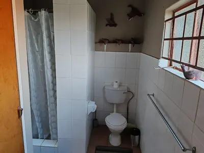 a white bathroom with a toilet and a window at 83 on De Lange in Graskop