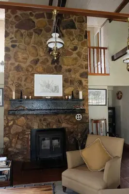 a living room with a stone fireplace and a chair at Eden Rain in Dullstroom