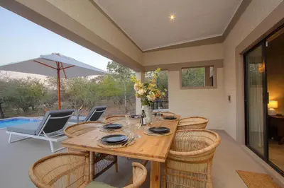 a wooden table with chairs and an umbrella on a patio at MRLTH Luxury Safari Villa, Close to KNP, Giraffe-Feeding-Tower, Spa-Bath, Boma in Marloth Park