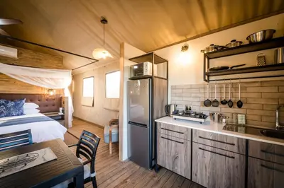a room with a bed and a kitchen with a refrigerator at Nkuhlu Tented Camp in Skukuza