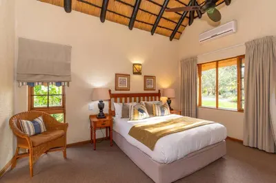 a bedroom with a bed and a chair and windows at Kruger Park Lodge Unit No. 254 in Hazyview