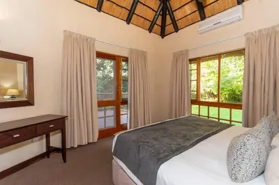 a bedroom with a bed and a desk and windows at Kruger Park Lodge Unit No. 254 in Hazyview