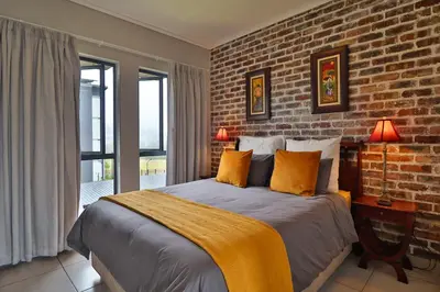 a bedroom with a large bed with a brick wall at Luxury Lowveld Apartment in Nelspruit