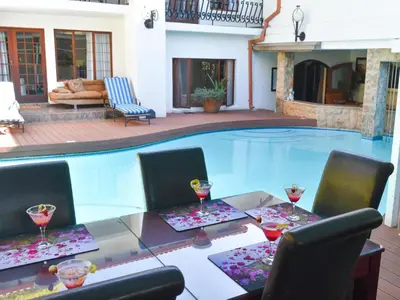 a pool with a table and chairs with wine glasses at Aanmani Rose Guesthouse in Pretoria