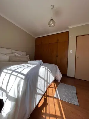a bedroom with a white bed with a wooden headboard at Ka Tembe Self Catering Lodge in Polokwane