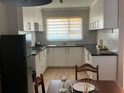 a kitchen with white cabinets and a table with a wine glass at Tintswalo Elegant Apartments in Giyani