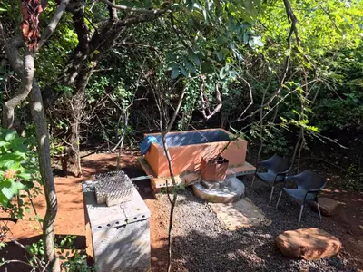 a bench and two chairs sitting in a forest at Hartbeest Bush Stay #3 in Hartbeespoort
