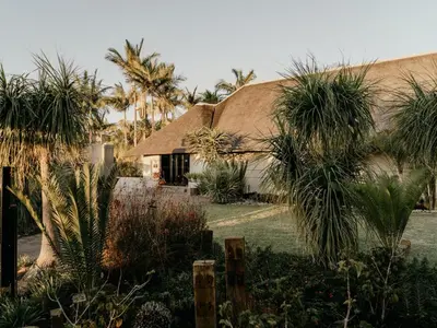 a house with a thatched roof and palm trees at Decollage Estate in Polokwane