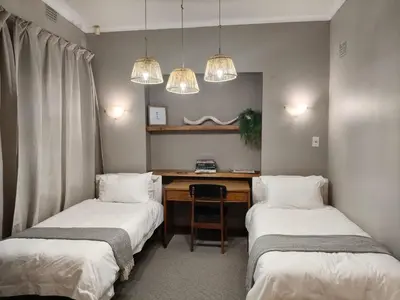 a room with two beds and a desk and two lights at The Bardolino Artists Retreat in Nelspruit