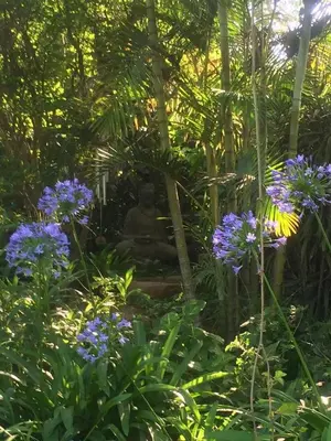 a buddha statue in a garden with purple flowers at The Bardolino Artists Retreat in Nelspruit