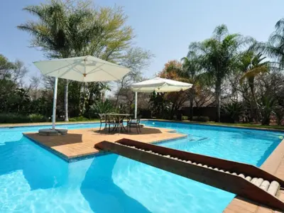 a swimming pool with a table and an umbrella at Mokuru Private Nature Reserve in Brits