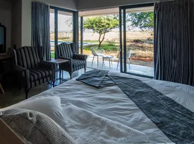 a bedroom with a bed and chairs and a large window at Sihlangu Lodge in Marloth Park