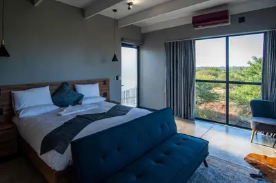 a bedroom with a blue bed and a large window at Sihlangu Lodge in Marloth Park