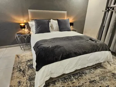 a bedroom with a large bed with a black blanket and pillows at Elson Manor Guesthouse in Tzaneen