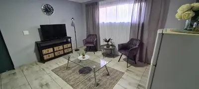 a living room with a tv and chairs and a table at Cozy Little Nest in Pretoria