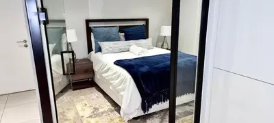 a bedroom with a bed with blue pillows and a mirror at Xquisite Ellipse Apartment in Midrand