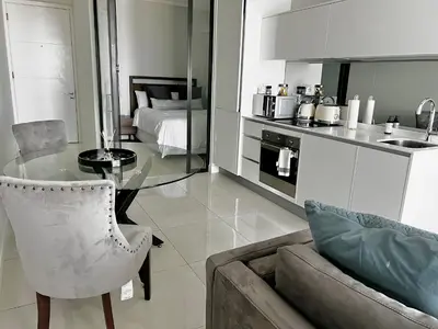 a living room with a glass table and a kitchen at Xquisite Ellipse Apartment in Midrand