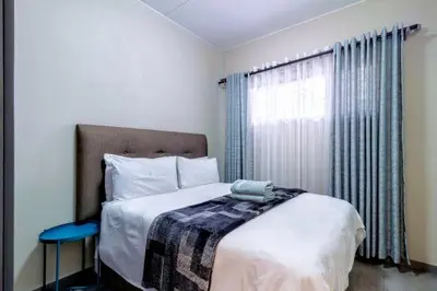 a bedroom with a bed with a blue stool and a window at The Waterfallcity Charm next to Mall of Africa in Midrand