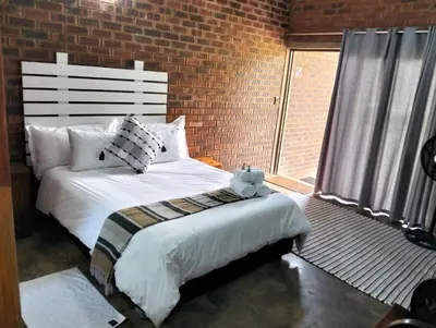 a bedroom with a white bed and a brick wall at Kataluma in Pretoria
