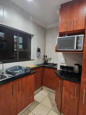 a kitchen with wooden cabinets and a microwave at Lily Rest Garden Cottage in Pretoria