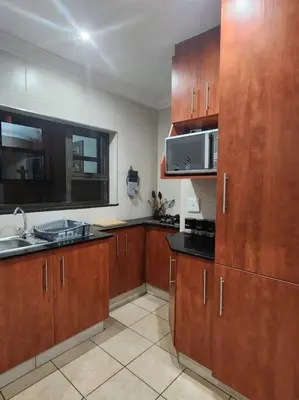 a kitchen with wooden cabinets and a sink and a microwave at Lily Rest Garden Cottage in Pretoria