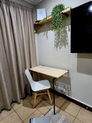 a desk with a white chair next to a television at Lily Rest Garden Cottage in Pretoria
