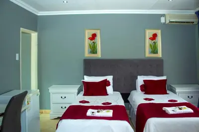 a bedroom with two beds with red and white sheets at Muofhe Graceland Lodge in Thohoyandou