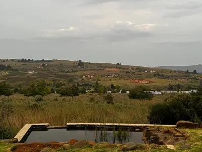 a pool of water in a field with a hill at iDube Lodge Walkersons in Dullstroom