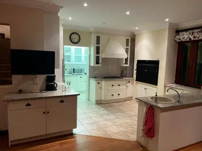 a kitchen with white cabinets and a clock on the wall at iDube Lodge Walkersons in Dullstroom